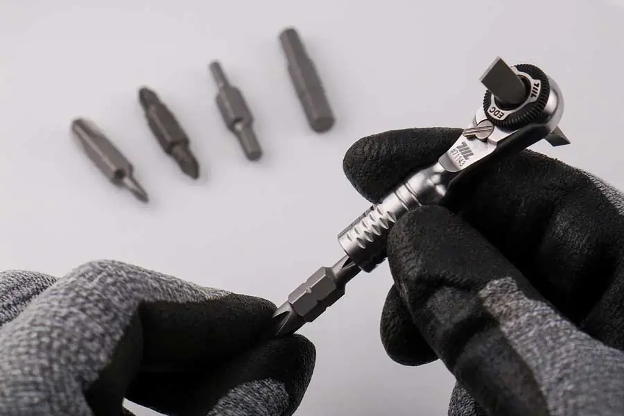 EDC Mini-Ratschenschlüssel in der Hand mit eingestecktem Bit und weiteren Bits im Hintergrund